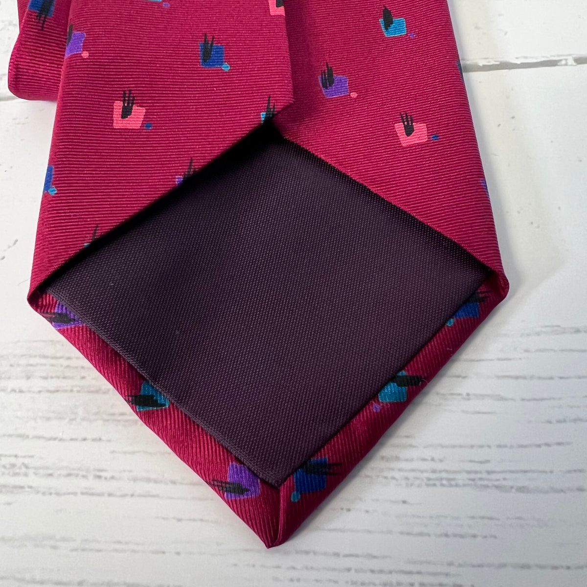 Red patterned tie with a dark pocket square on a light wooden surface