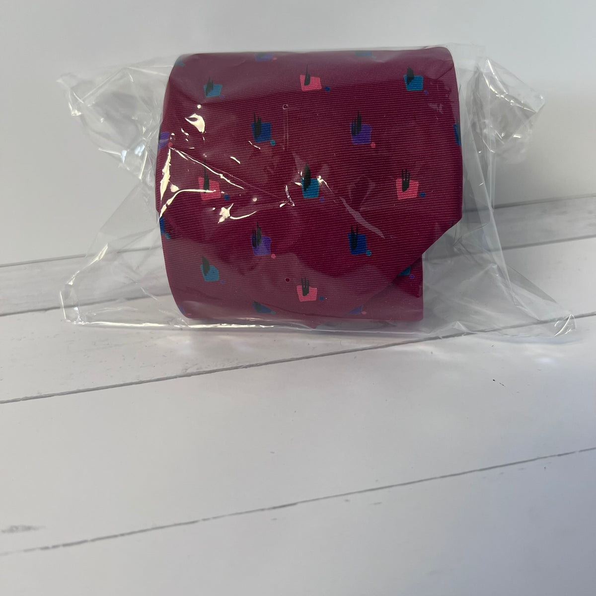 Red tie with blue and pink pattern in clear packaging on a white wooden surface