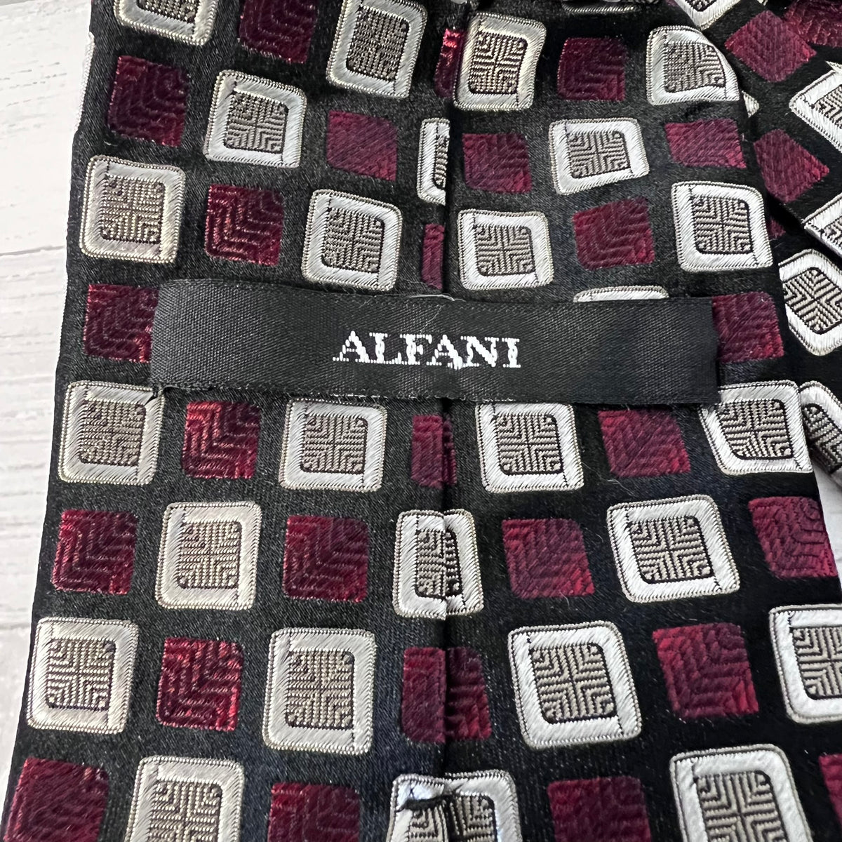 Patterned tie with geometric design and 'Alfani' label on a wooden surface
