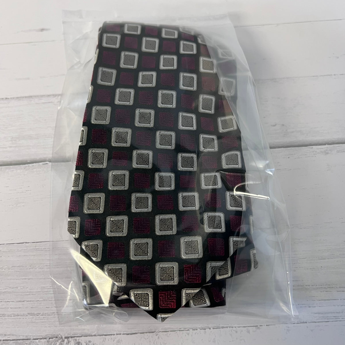 Patterned tie in a clear plastic bag on a light wooden surface