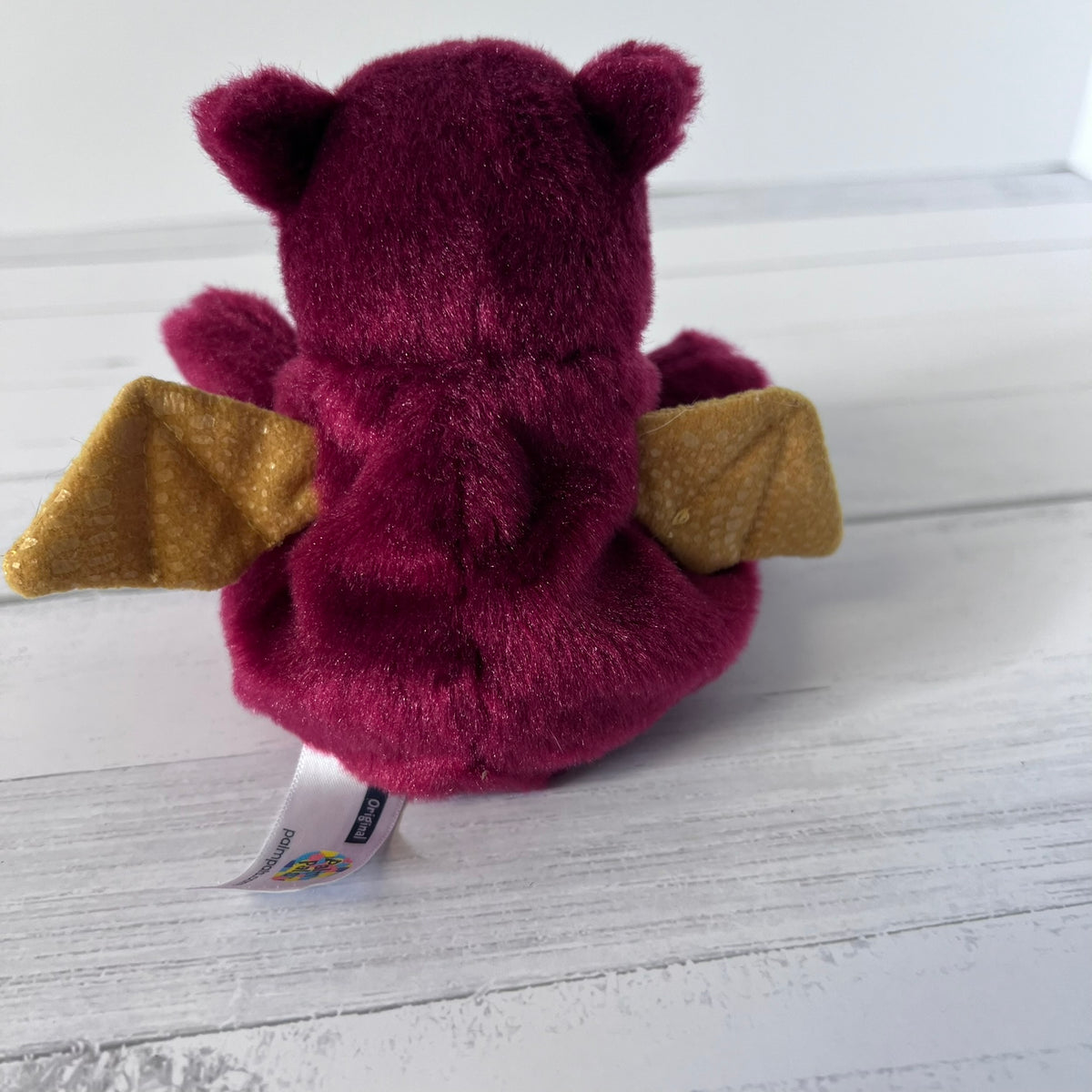Plush toy dragon with gold wings on a white wooden surface