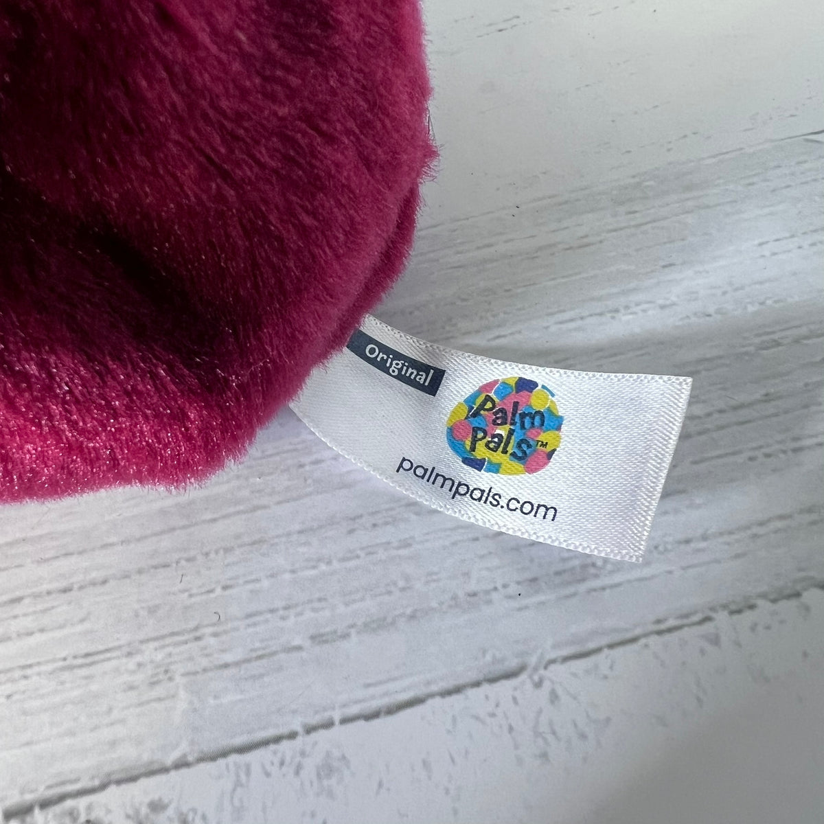 Close-up of a maroon plush toy with a 'Palmpals' label on a light wooden surface.