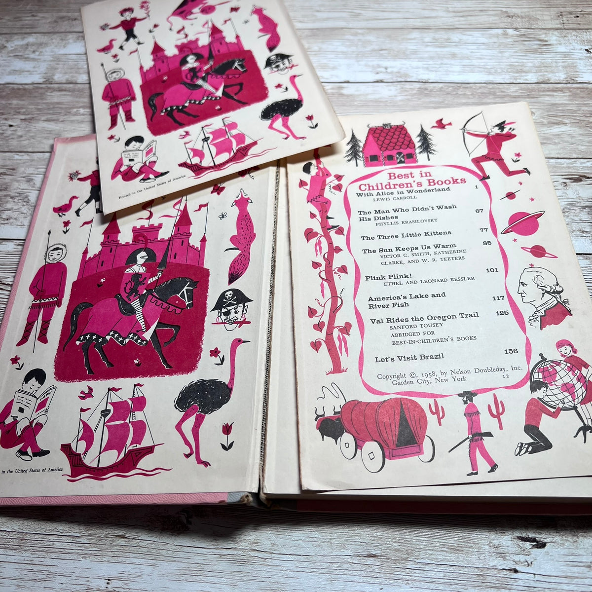 Vintage children's book set with illustrated covers and an open menu/book page, photographed on a light wood surface. The pages show pink and black drawings on cream paper, including whimsical characters, a castle, ships, and a book list.