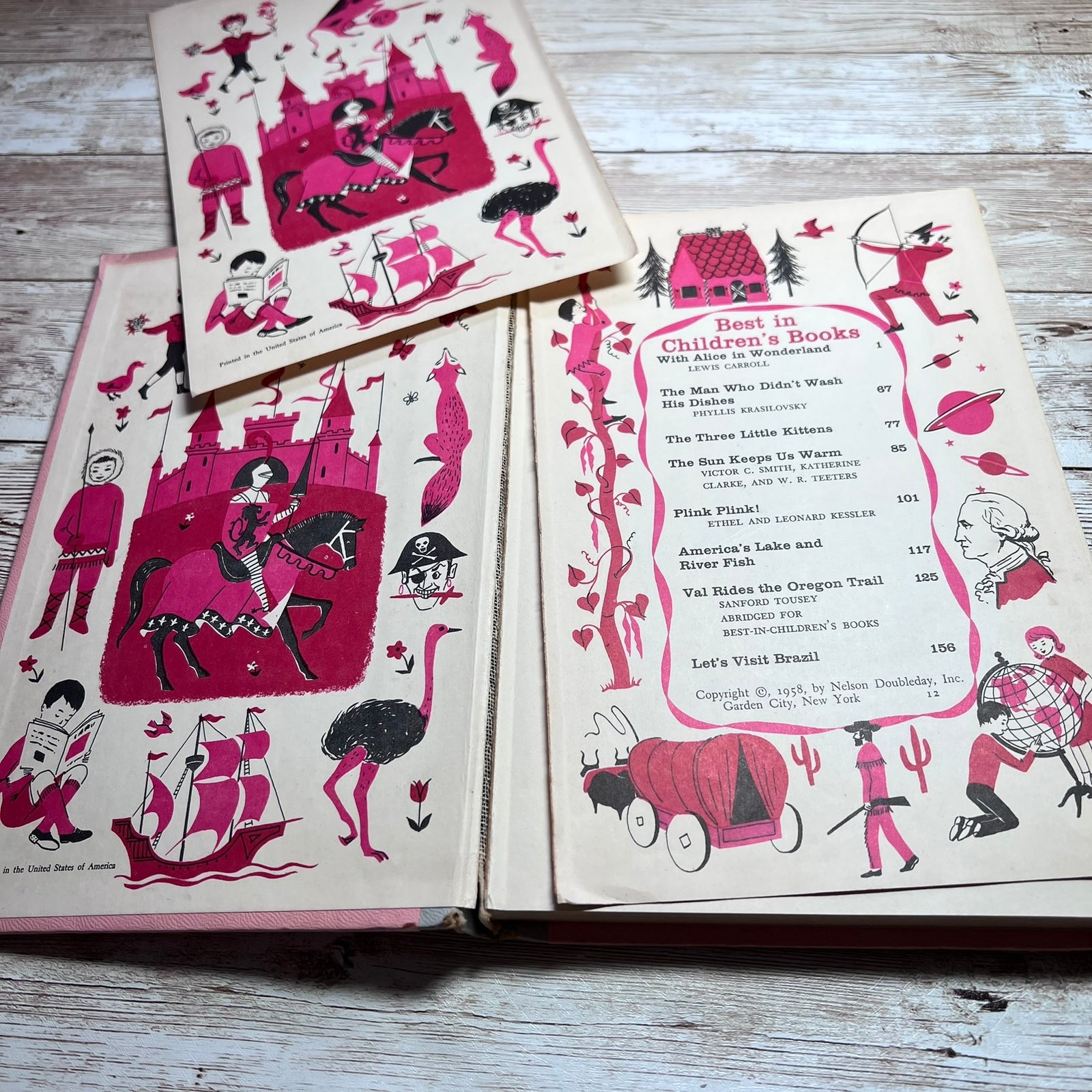 Vintage children's book set with illustrated covers and an open menu/book page, photographed on a light wood surface. The pages show pink and black drawings on cream paper, including whimsical characters, a castle, ships, and a book list.