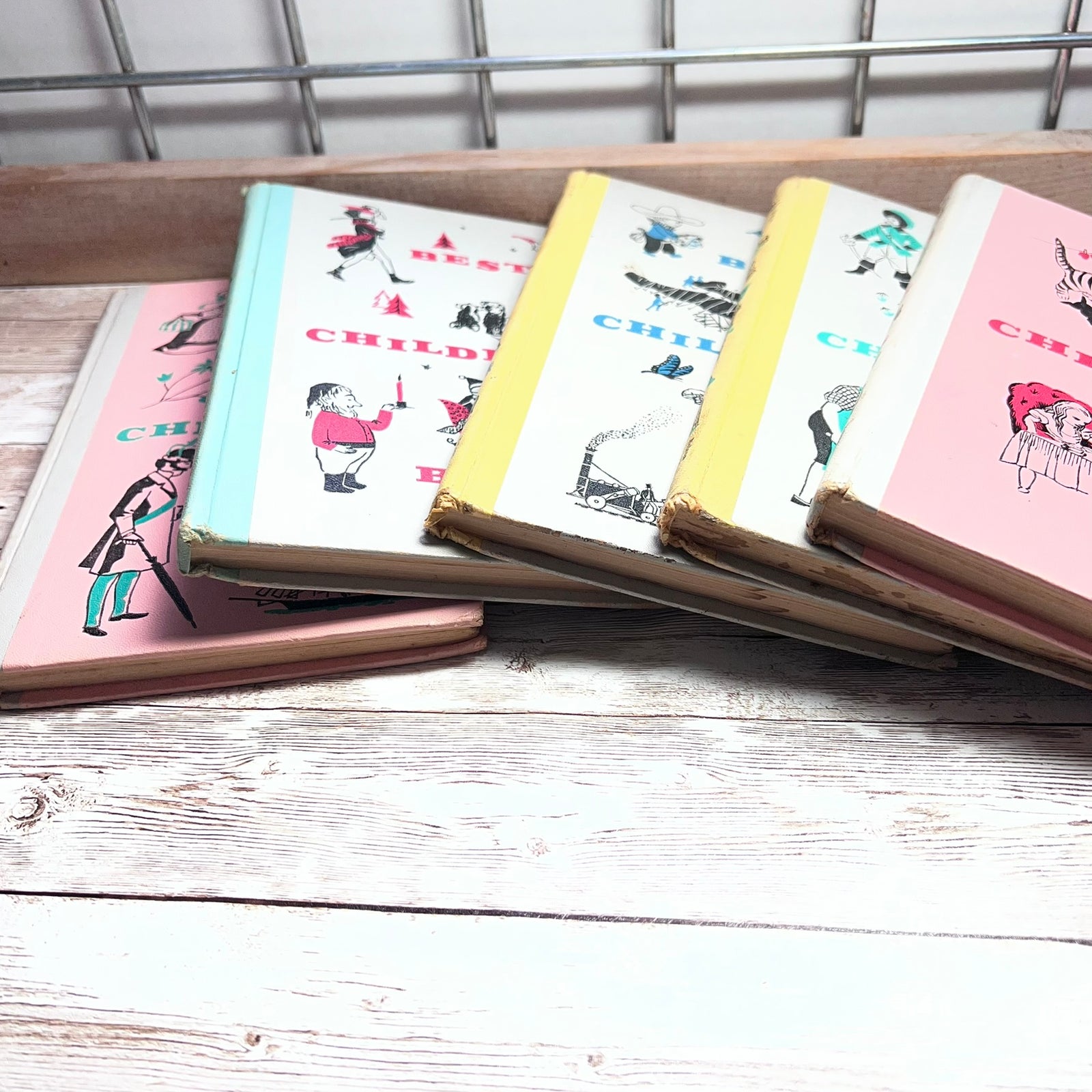 A set of vintage children's picture books fanned out on a white wooden surface, featuring pastel-colored covers with illustrations of children and the word 'CHILDREN'.