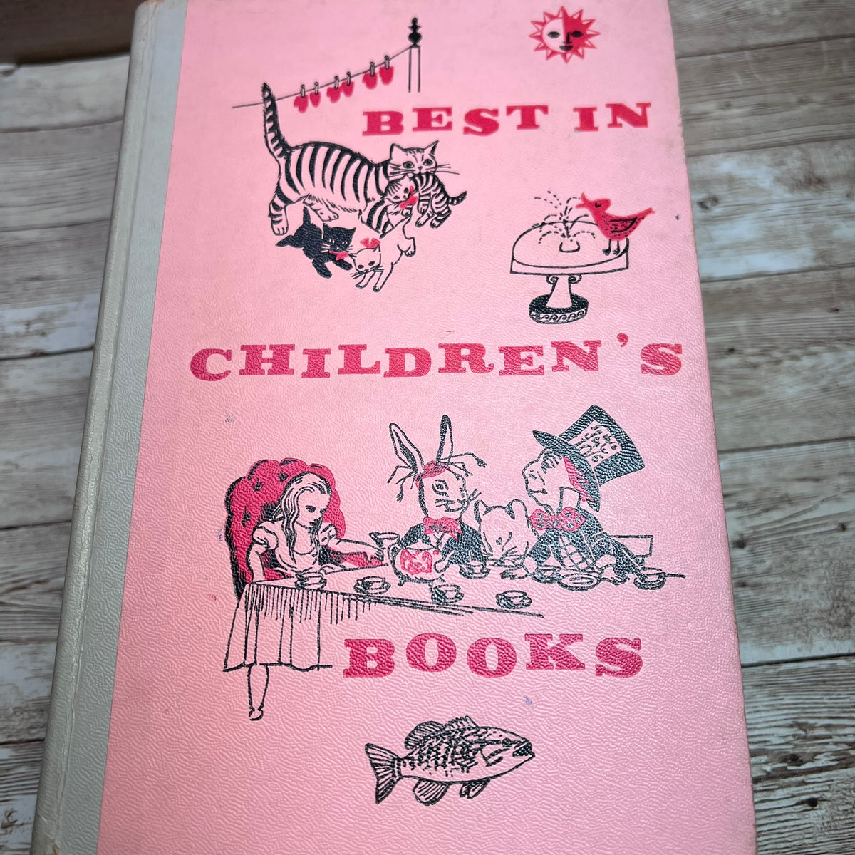 A vintage pink children's book or book cover titled "Best in Children's Books," featuring illustrated animals and characters in black and red on a wood surface.