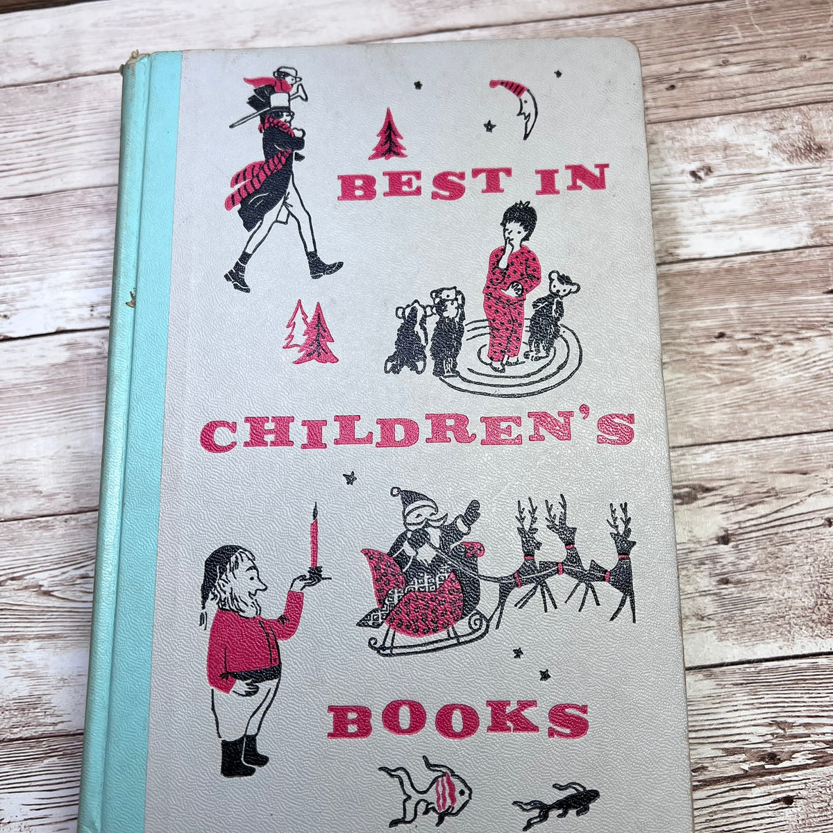 Vintage hardcover children's book titled 'Best in Children's Books' with illustrated holiday scenes on a light cover and a pale blue spine, photographed on a rustic wood surface.