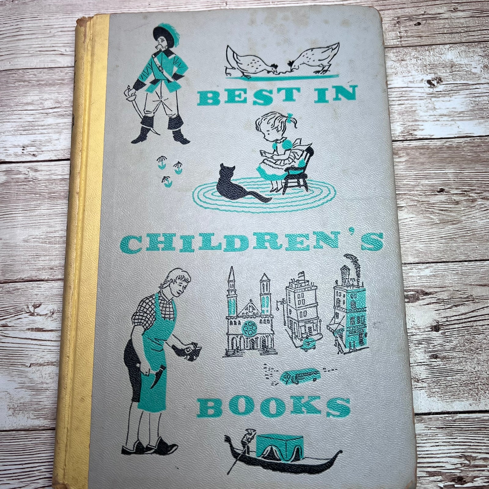 Vintage children's book with a light gray cover featuring teal and black illustrations and the title 'BEST IN CHILDREN'S BOOKS,' photographed on a rustic wood surface.