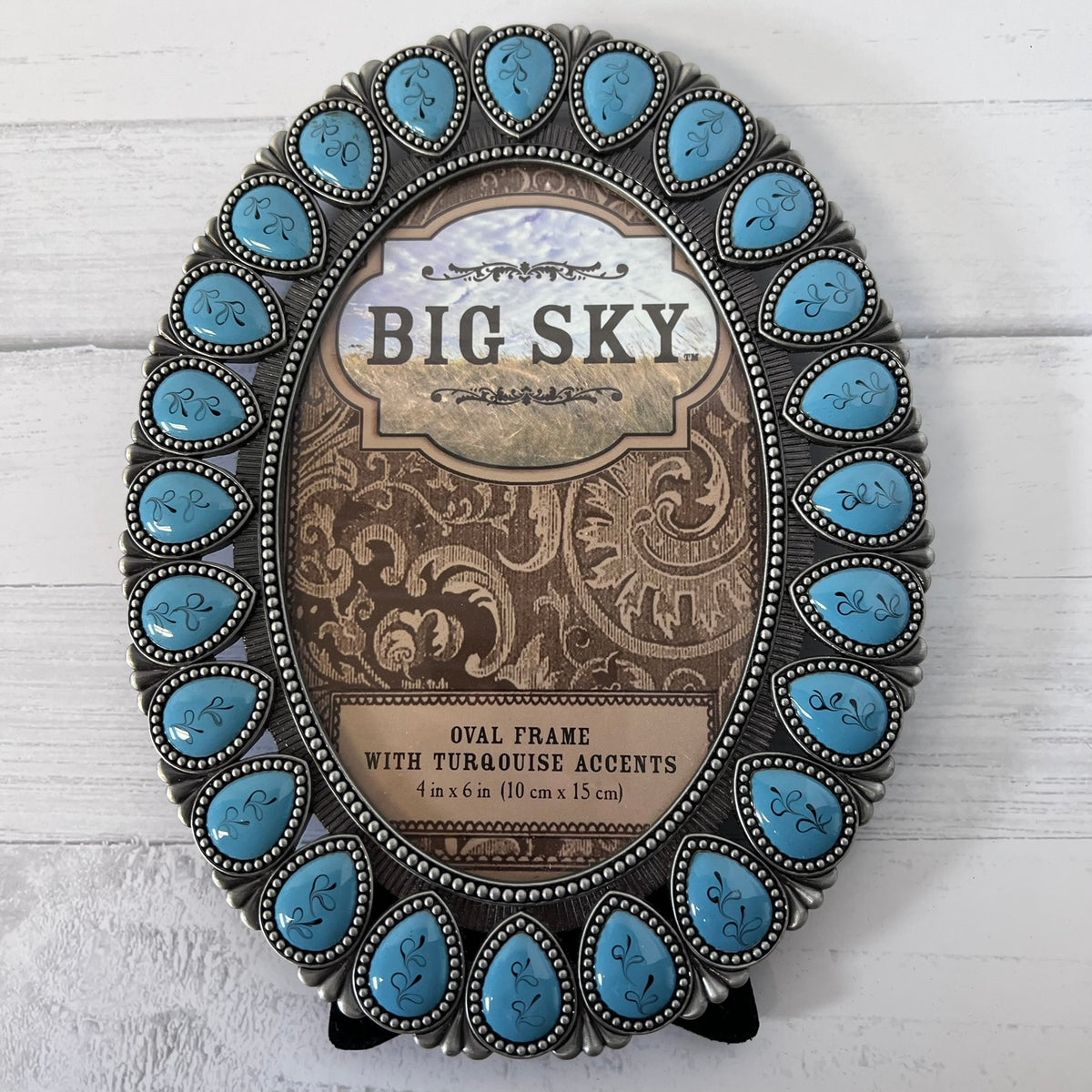 Oval decorative picture frame with a silver-toned Southwestern-style border and turquoise stone accents, shown on a white wood background. The center insert reads “BIG SKY.