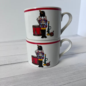Two stacked mugs with nutcracker design on a light wooden surface