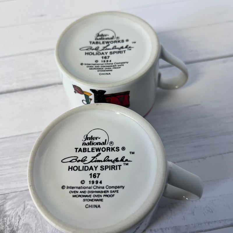 Two white mugs with  branding on a light wooden surface