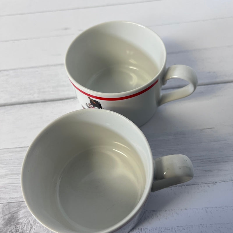 Two white mugs with red stripes on a light wooden surface
