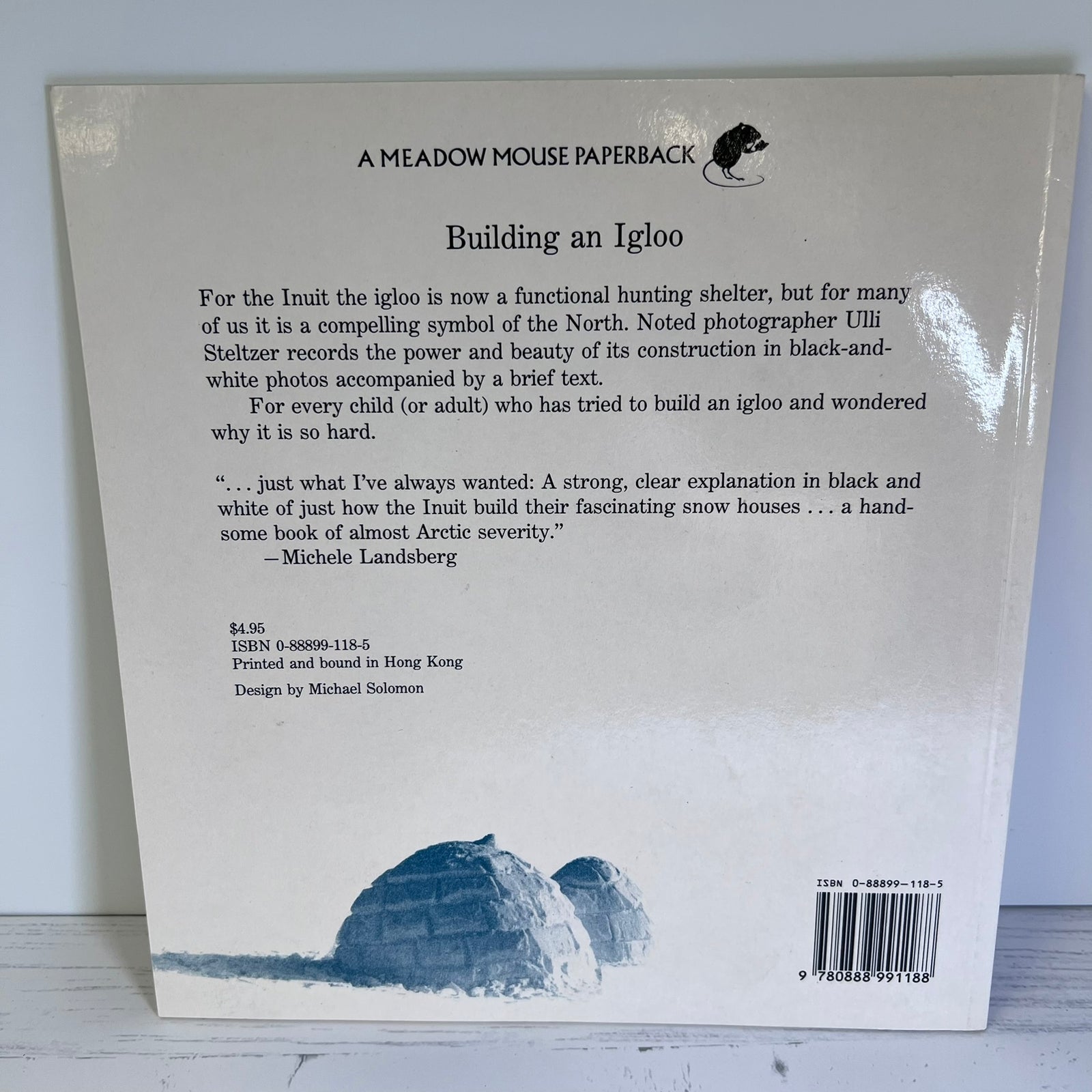 The back cover of a paperback book titled 'Building an Igloo' by Design by Michael Solomon, published by Meadow Mouse Paperbacks. The white cover features black text, a small black bear logo at the top, and a blue-toned illustration of an igloo at the bottom.