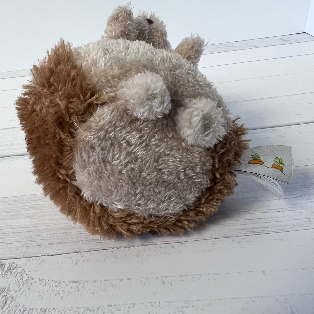Plush hedgehog toy with a tag on a light wooden floor