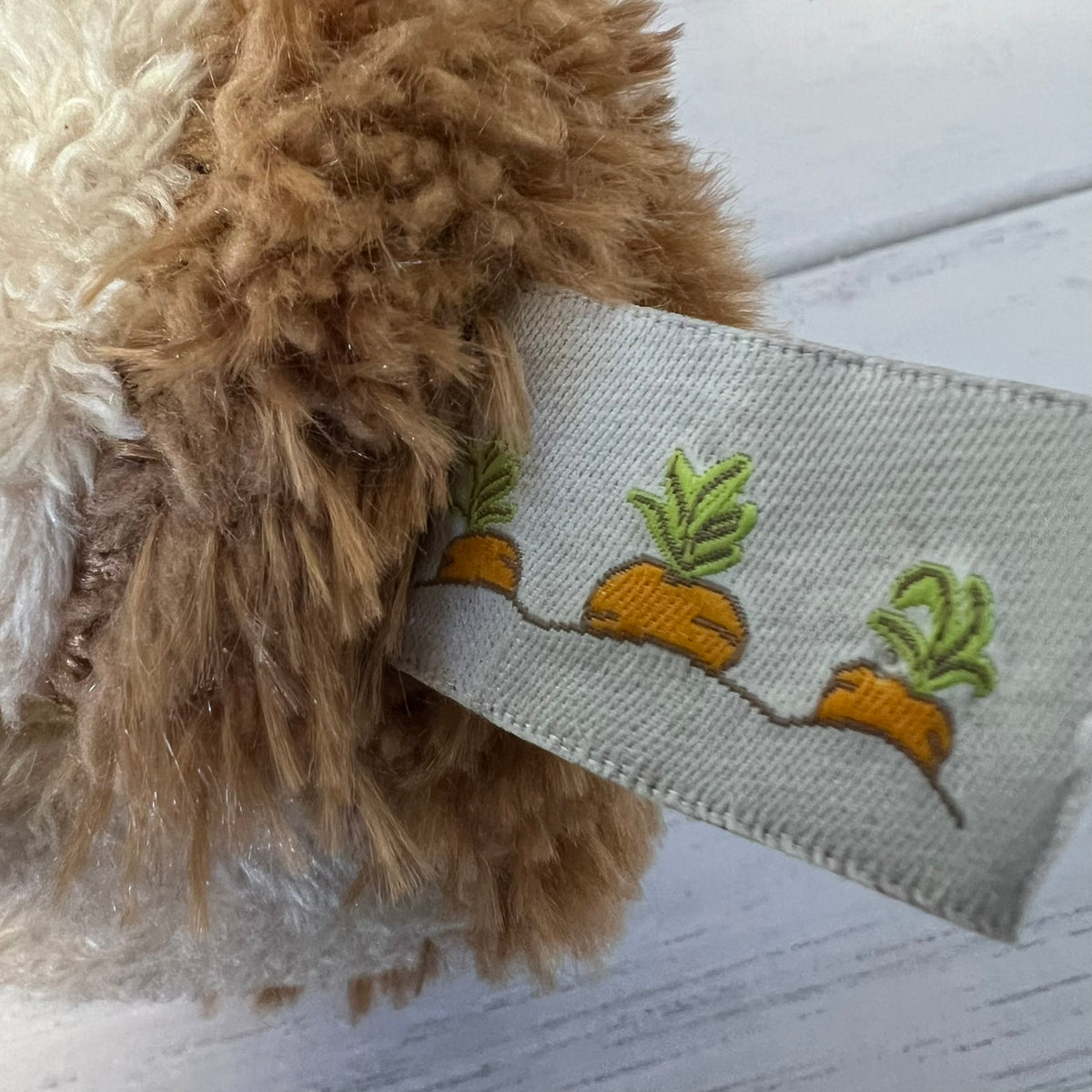 Close-up of a plush toy with an embroidered label featuring plants on a light wooden surface.
