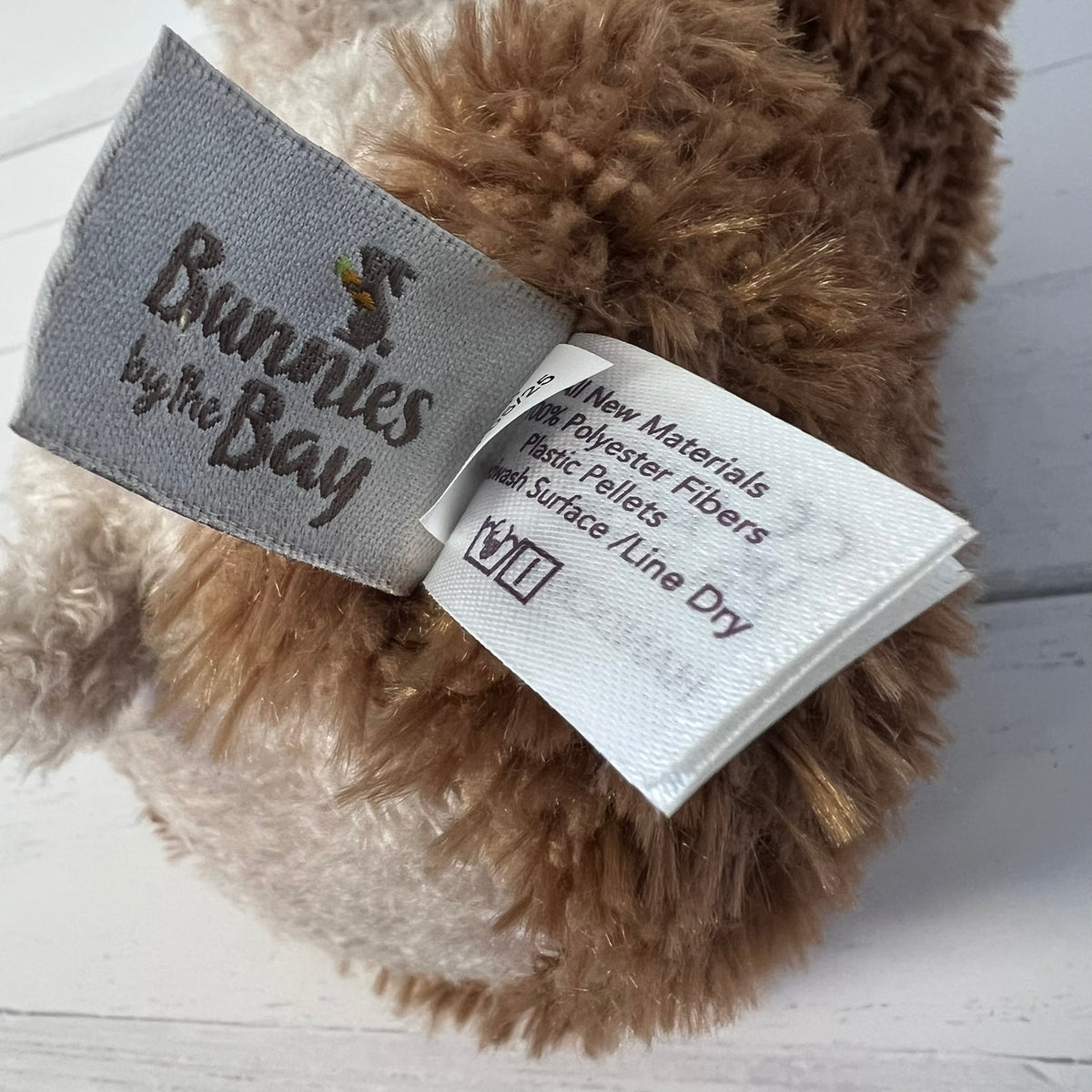 Close-up of a plush toy with a label and 'Bunnies by the Bay' branding on a wooden surface.