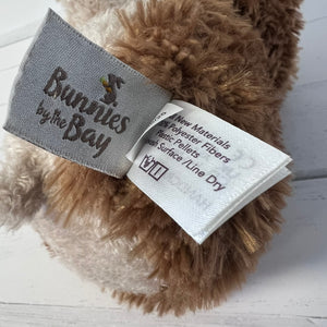 Close-up of a plush toy with a label and 'Bunnies by the Bay' branding on a wooden surface.