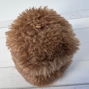 Brown fluffy pom-pom on a white wooden surface