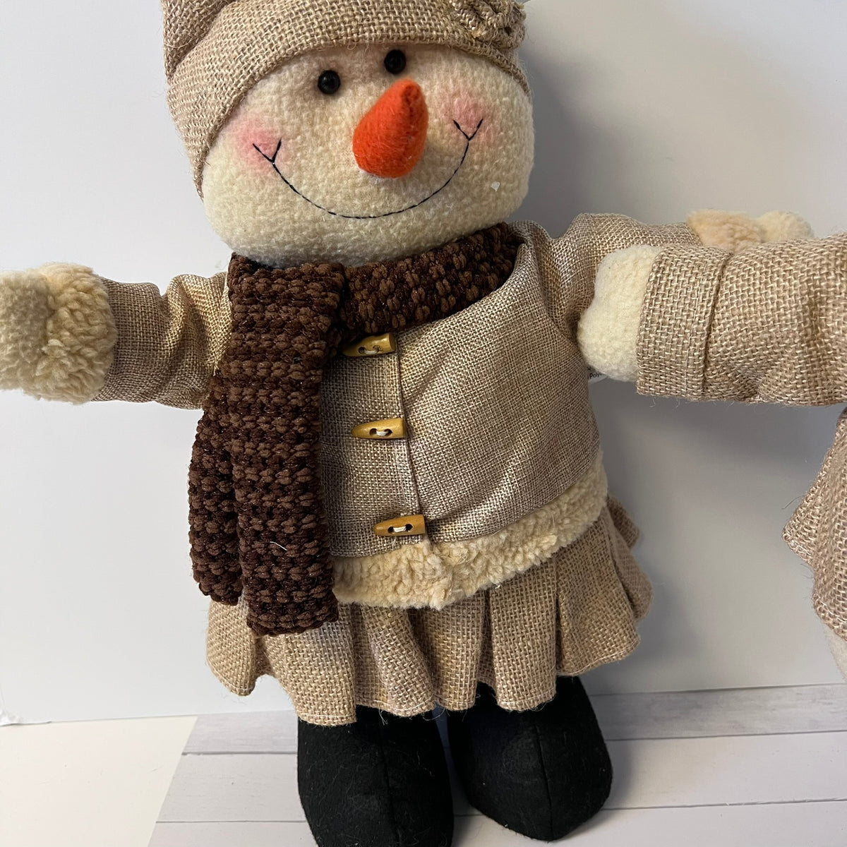 Plush snowman toy with a brown coat, scarf, and hat on a white background