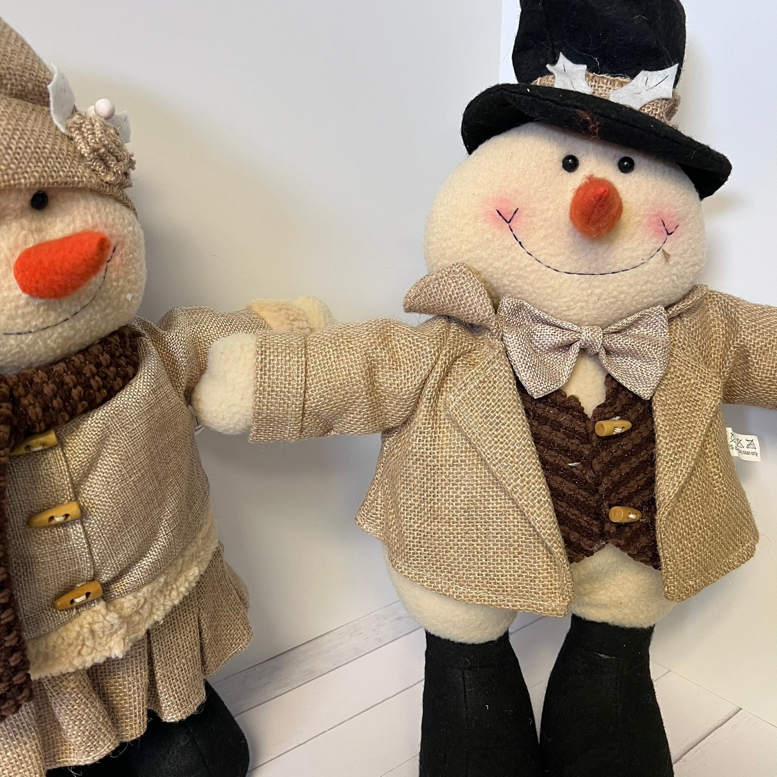 Two plush snowmen dressed in winter clothing on a white floor.