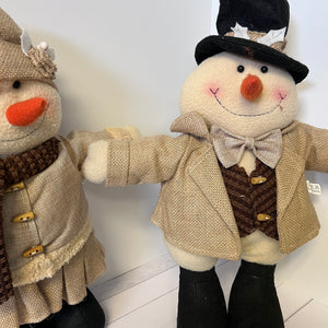 Two plush snowmen dressed in winter clothing on a white floor.