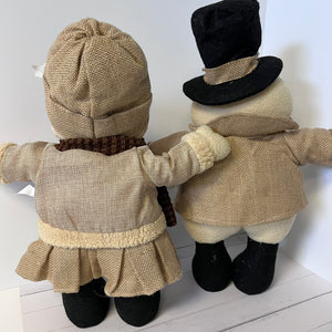 Two toy figures dressed in vintage-style clothing, including hats and coats, standing against a white background.