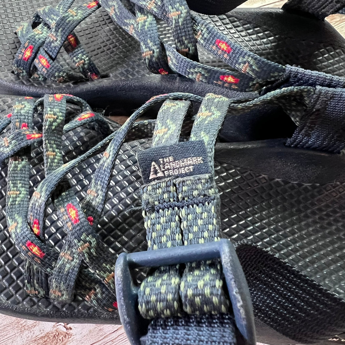 Close-up of a pair of Larchmont & Project athletic sandals with dark textured soles and patterned straps in green, gray, and red.