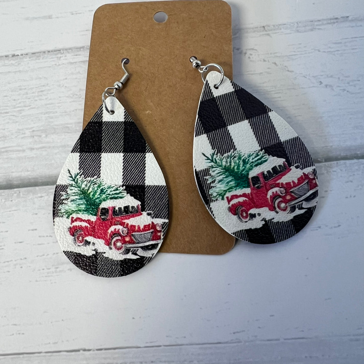 Teardrop-shaped earrings with black and white plaid design featuring a red truck and Christmas tree on a brown card.