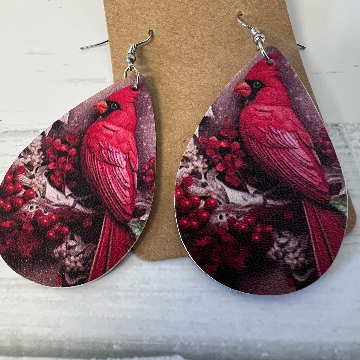 Teardrop-shaped earrings with red cardinal birds and berries on a brown card.