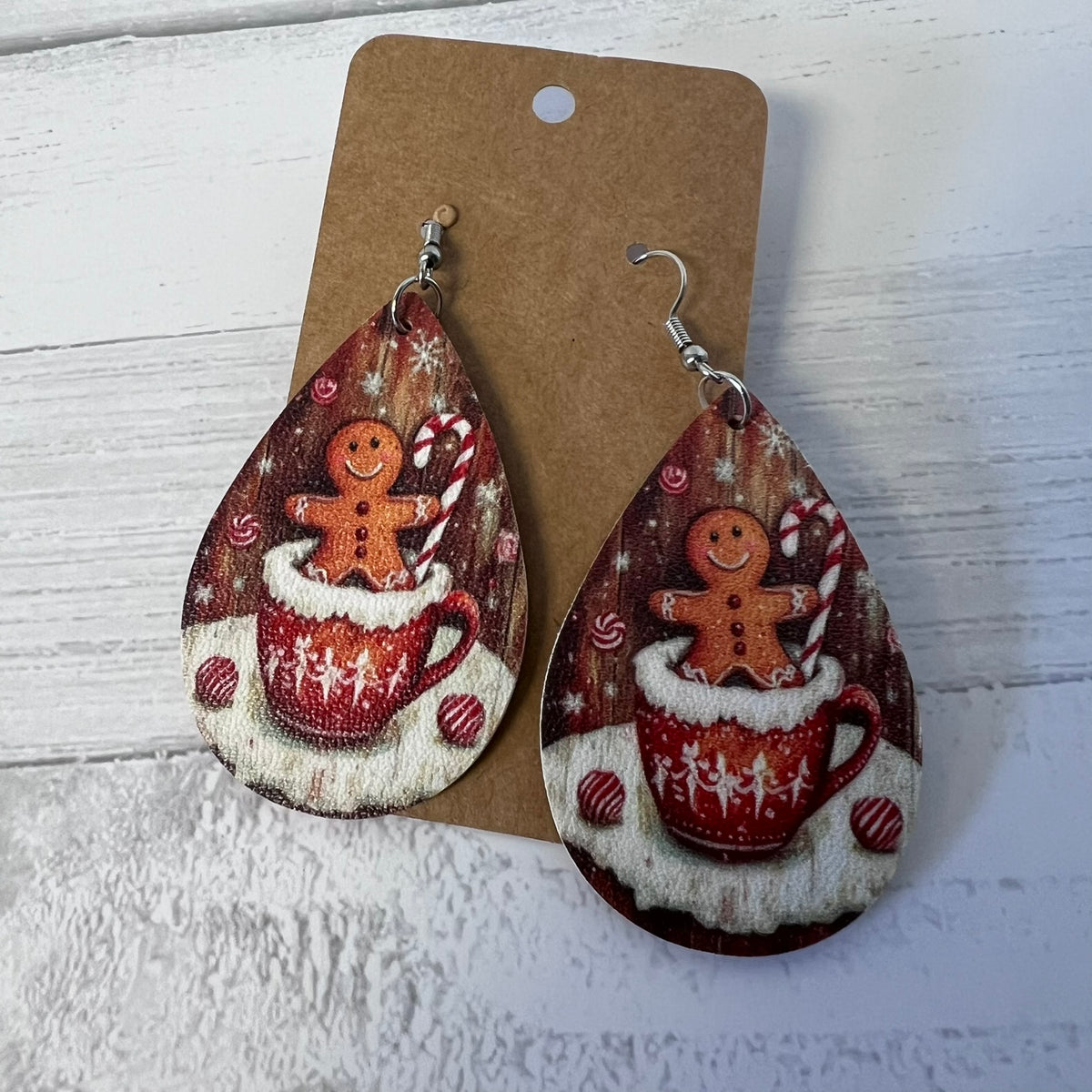 Teardrop-shaped earrings with gingerbread man and hot chocolate design on a cardboard backing.