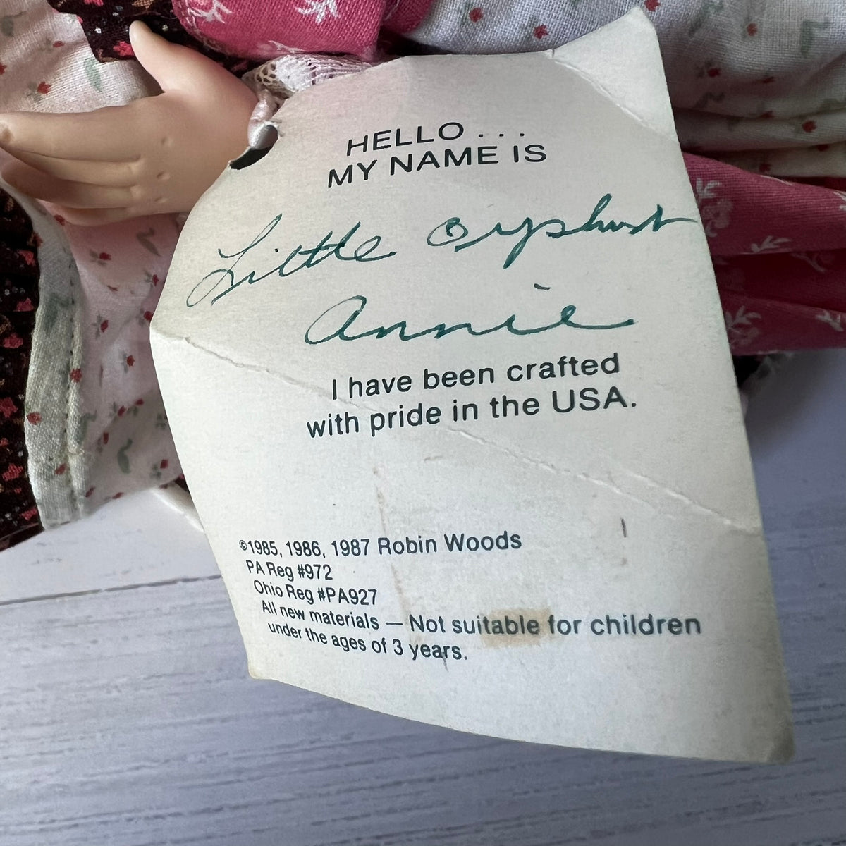 A vintage doll tag attached to a doll, reading 'HELLO.