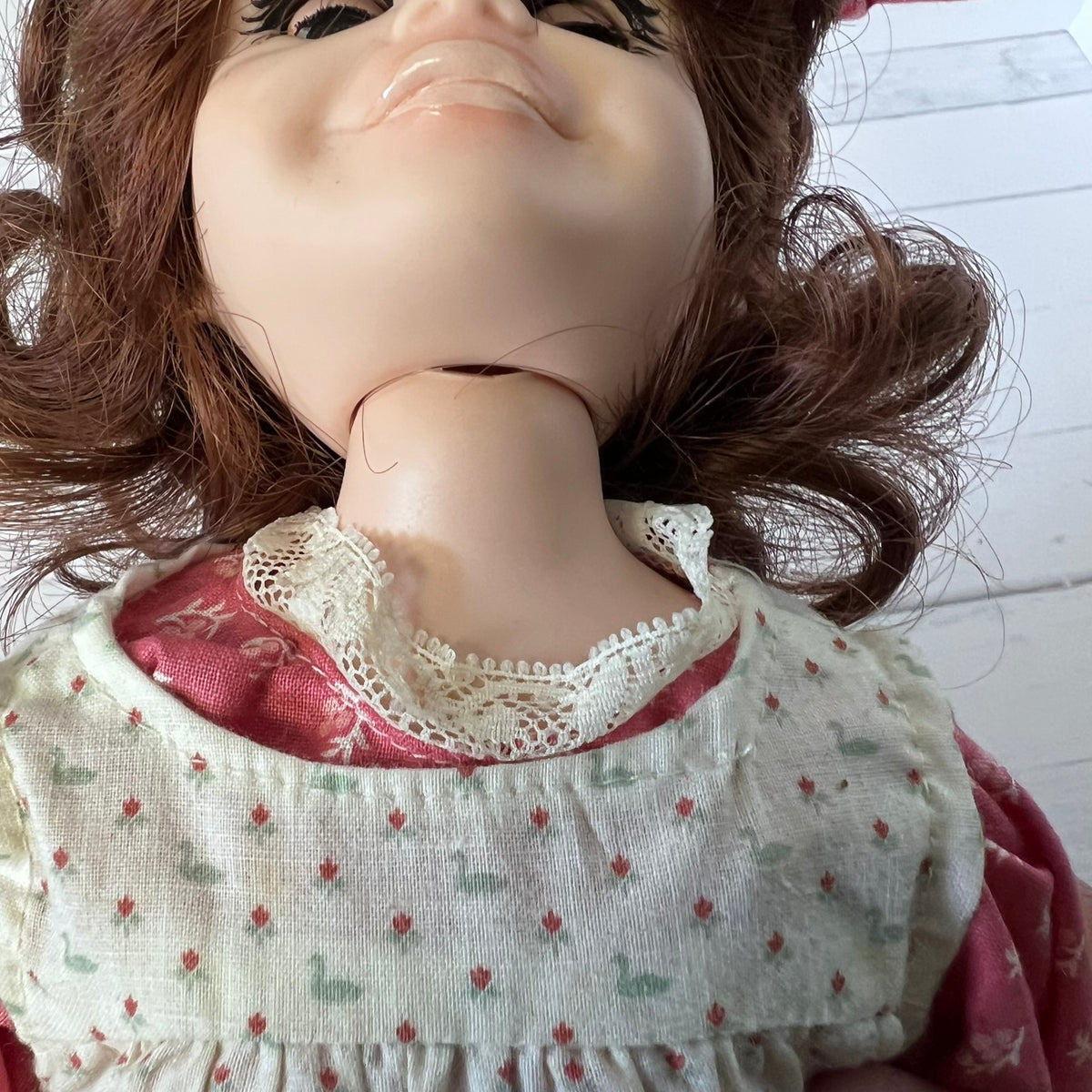 Close-up of a doll's lower face and neck wearing a cream bib with a small duck print and a pink dress underneath.