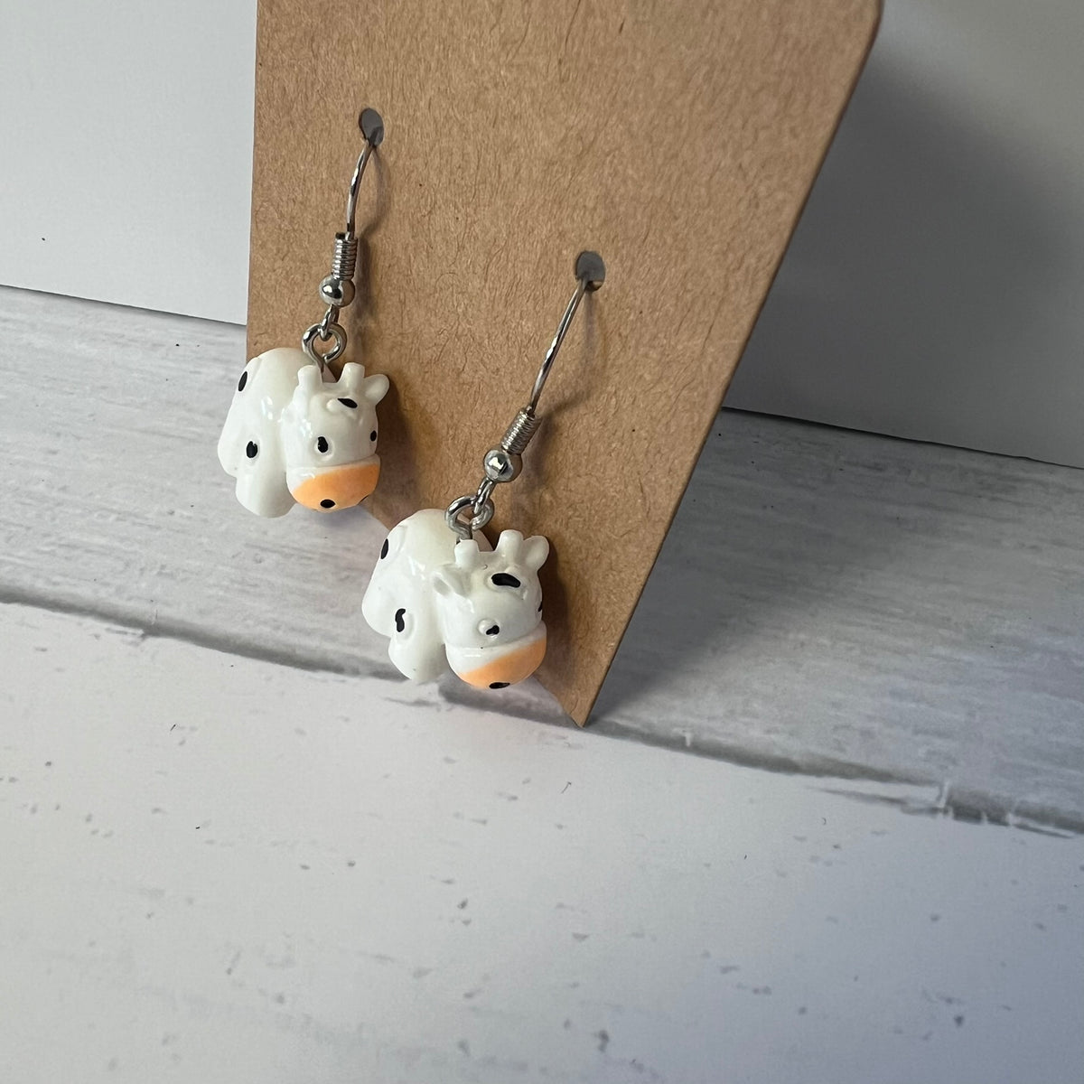 Pair of cow-shaped earrings on a cardboard backing against a light gray background