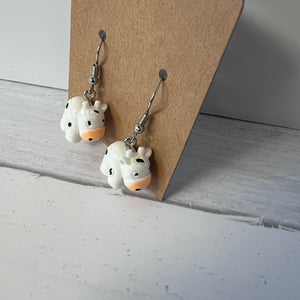 Pair of cow-shaped earrings on a cardboard backing against a light gray background