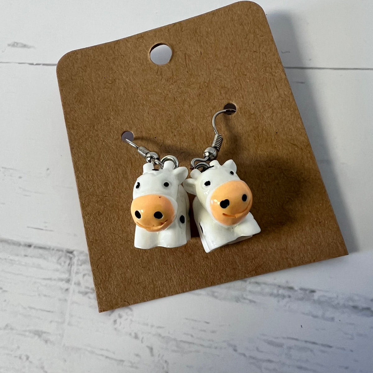 Cow-shaped earrings on a brown card with a white background