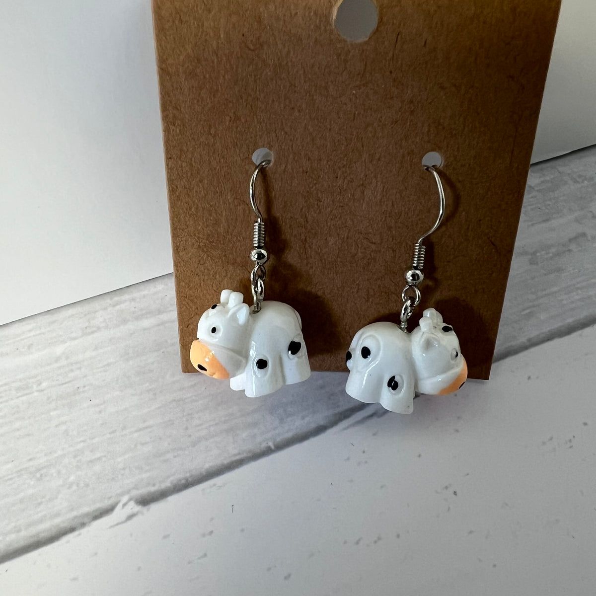 Pair of ghost-shaped earrings on a brown card against a white background