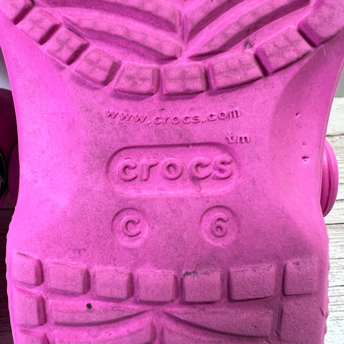 Close-up of the sole of a pink Crocs shoe, showing the embossed Crocs logo, website, size markings, and tread pattern.