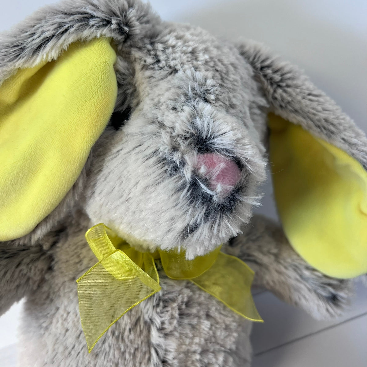 Close-up of a plush toy rabbit with yellow ears and bow tie on a light background