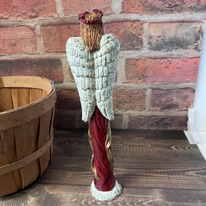 Decorative angel figurine with red robe and white wings against a brick wall.