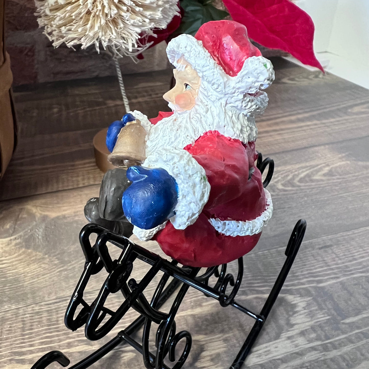 Decorative figure of Santa Claus on a sleigh with a bell, surrounded by festive decorations.