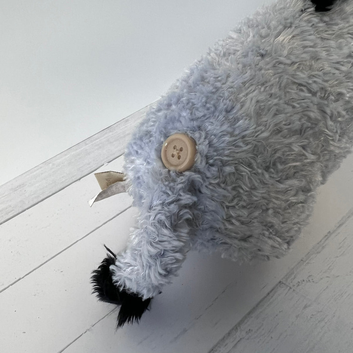 Gray plush toy with a button on a light wooden floor