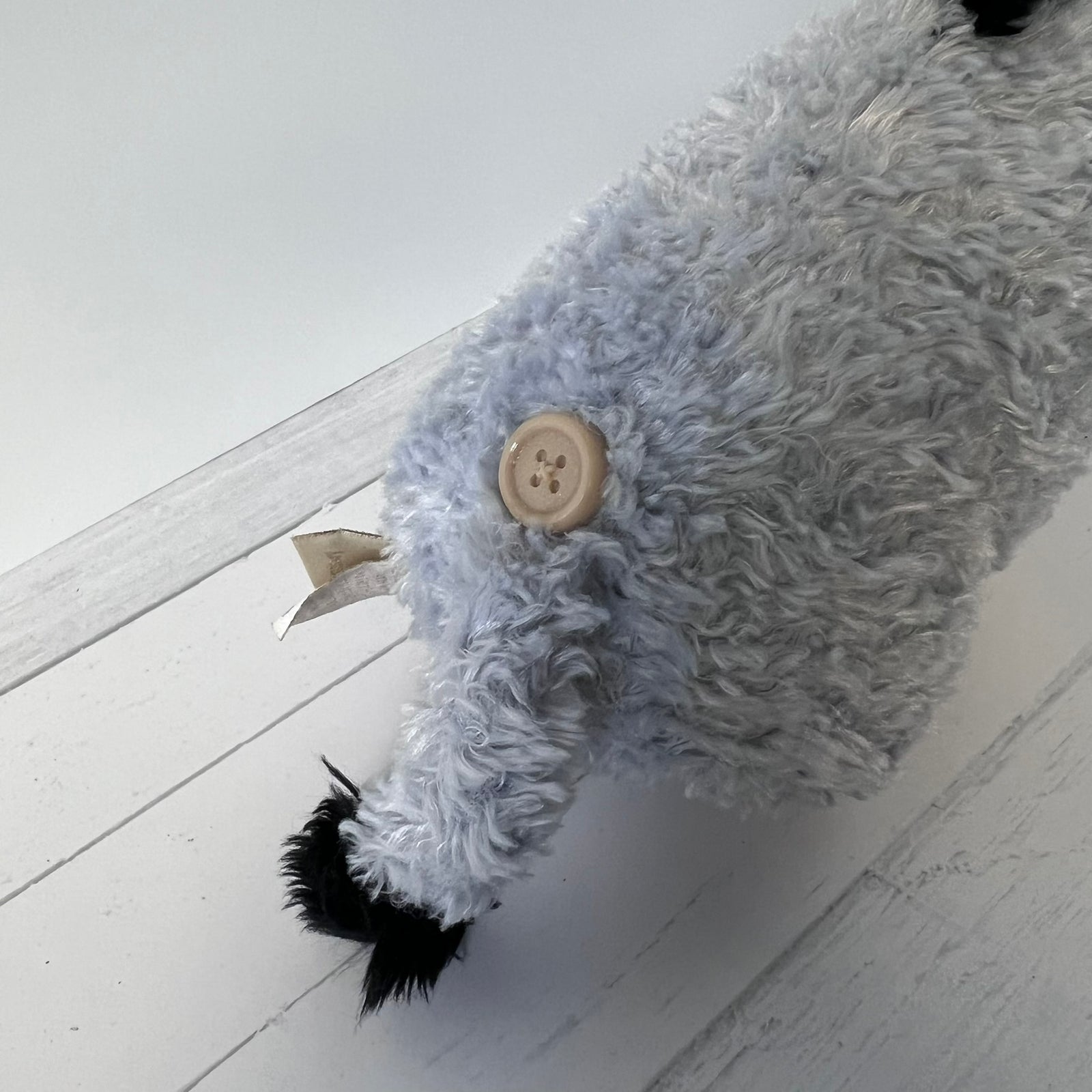 Gray plush toy with a button on a light wooden floor