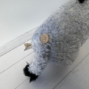 Gray plush toy with a button on a light wooden floor