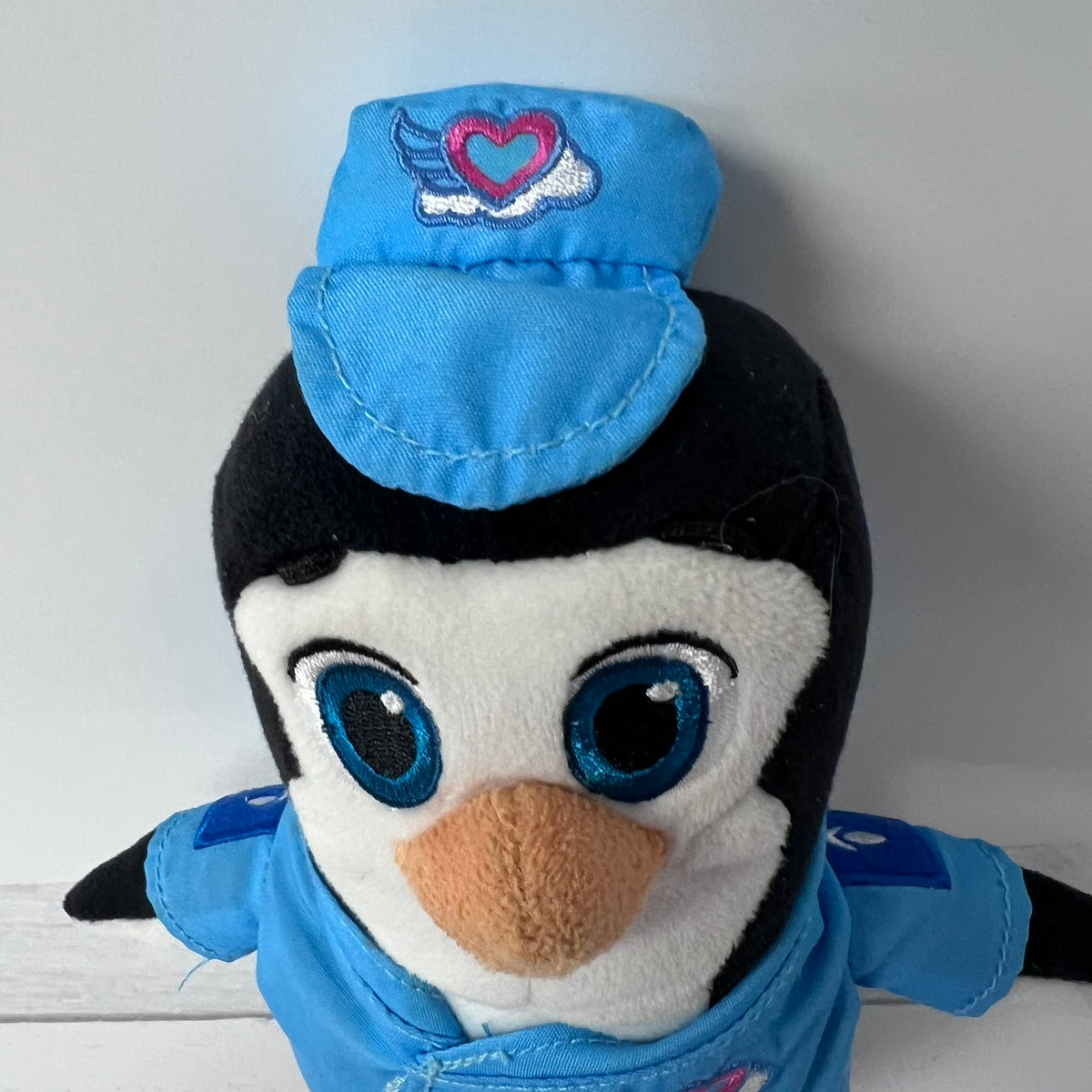 Plush penguin toy wearing a blue outfit with a heart emblem on a white background