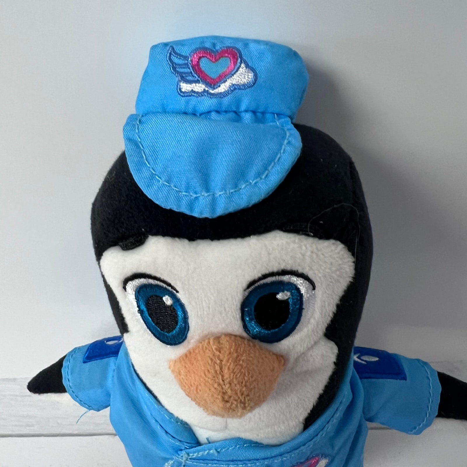 Plush penguin toy wearing a blue outfit with a heart emblem on a white background