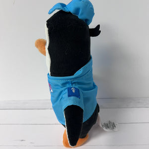 Plush toy resembling a penguin wearing a blue outfit on a white wooden floor.