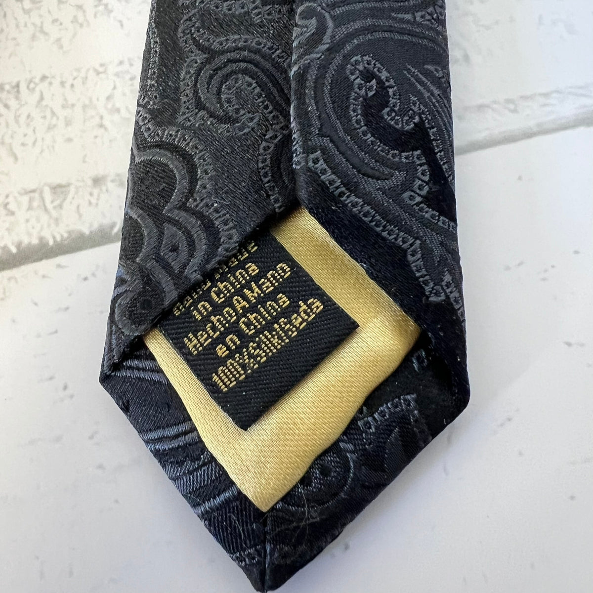Black patterned tie with a gold label on a white background
