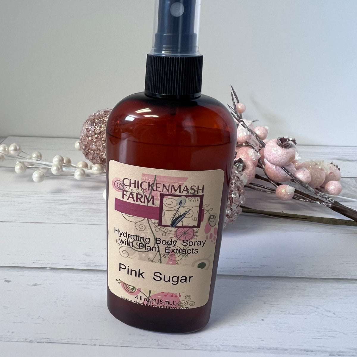 Brown bottle of Chickenmash Farm Pink Sugar body spray on a white surface with decorative elements.