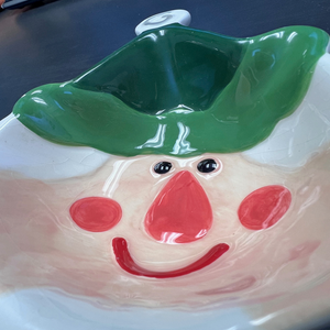 Ceramic bowl shaped like a smiling face with a green lid on a dark background