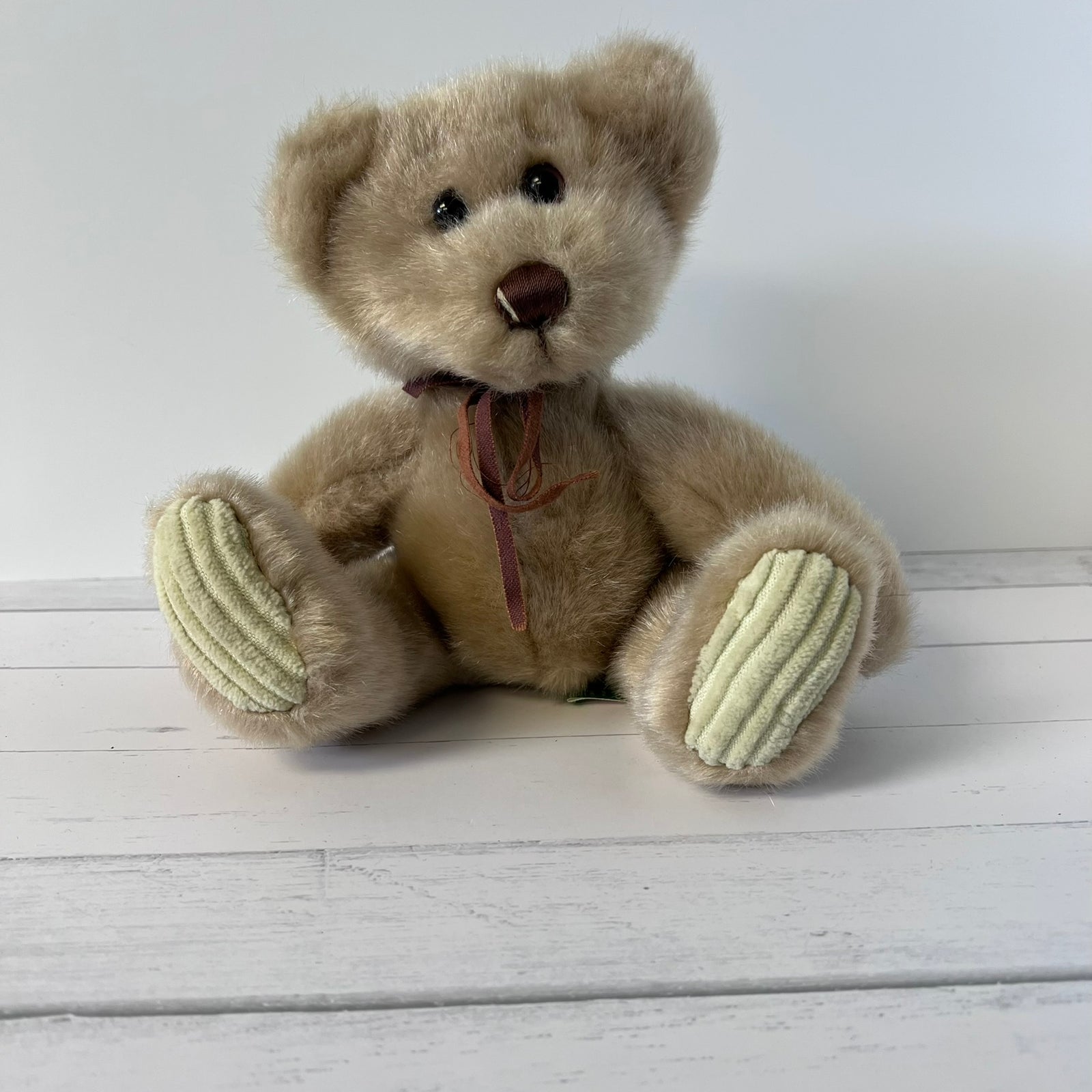 Beige teddy bear with a brown ribbon on a white wooden surface